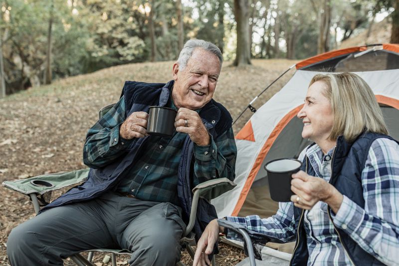 Happy senior having coffee on a camping trip in front of their tent.