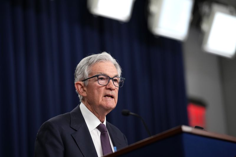 Jerome Powell stands in front of a podium, with curtains behind him during a press conference.