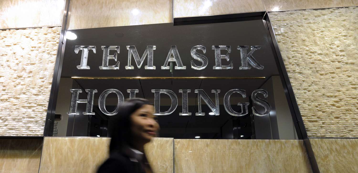 An employee walks past the logo of Temasek Holdings Pte at the company's headquarters, in Singapore