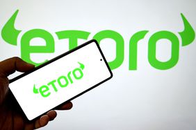 An eToro logo is seen displayed on a smartphone and in the background