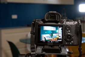 A camera on a tripod capturing a modern kitchen setup seen on its display screen, perspective from behind the camera.