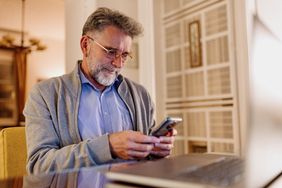 Person looking at smartphone while working in front of a laptop from home office