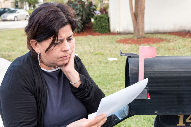 Woman by mailbox, reading letter with bad news