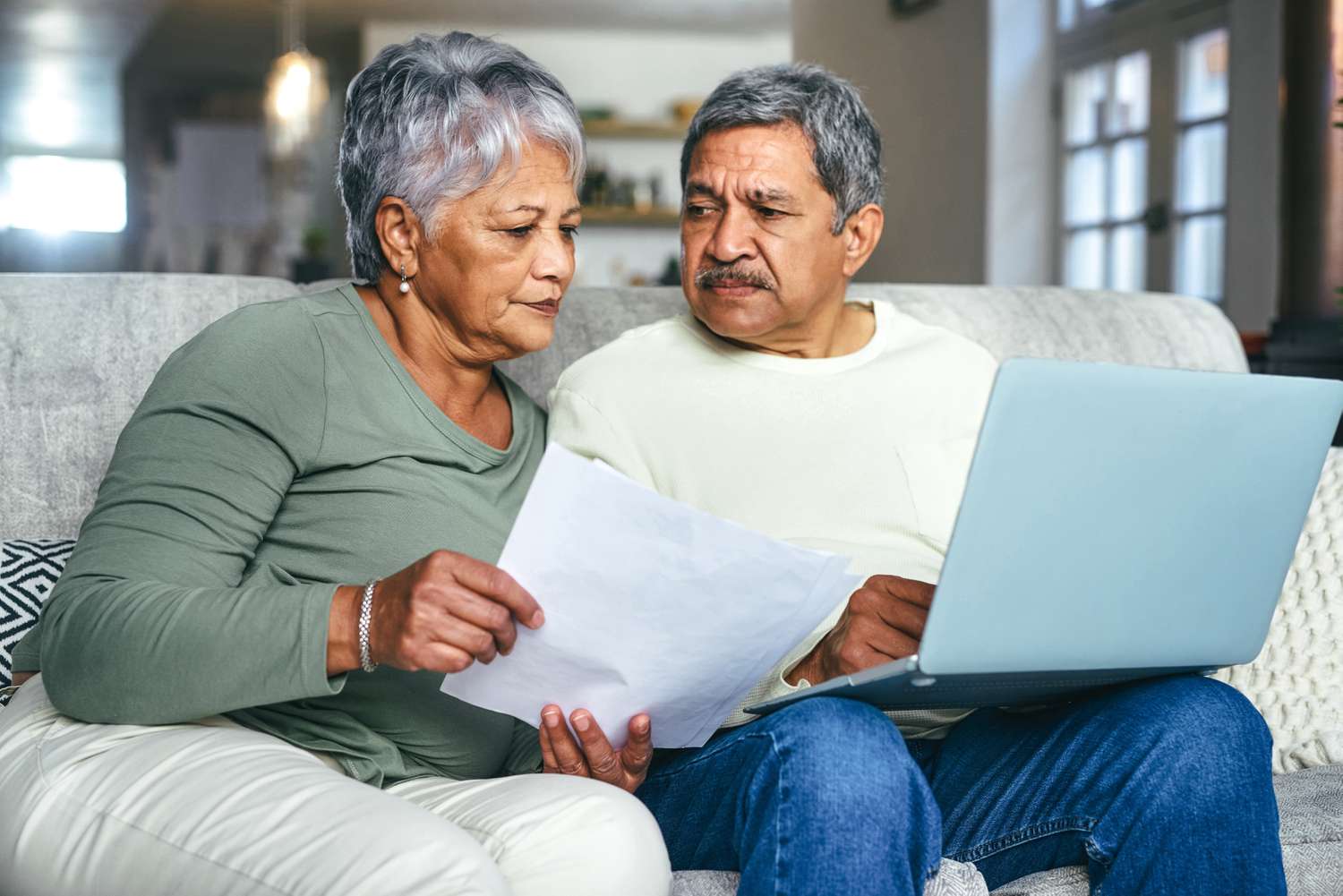 Older couple sitting on their sofa and looking with concern at a mortgage document and a laptop