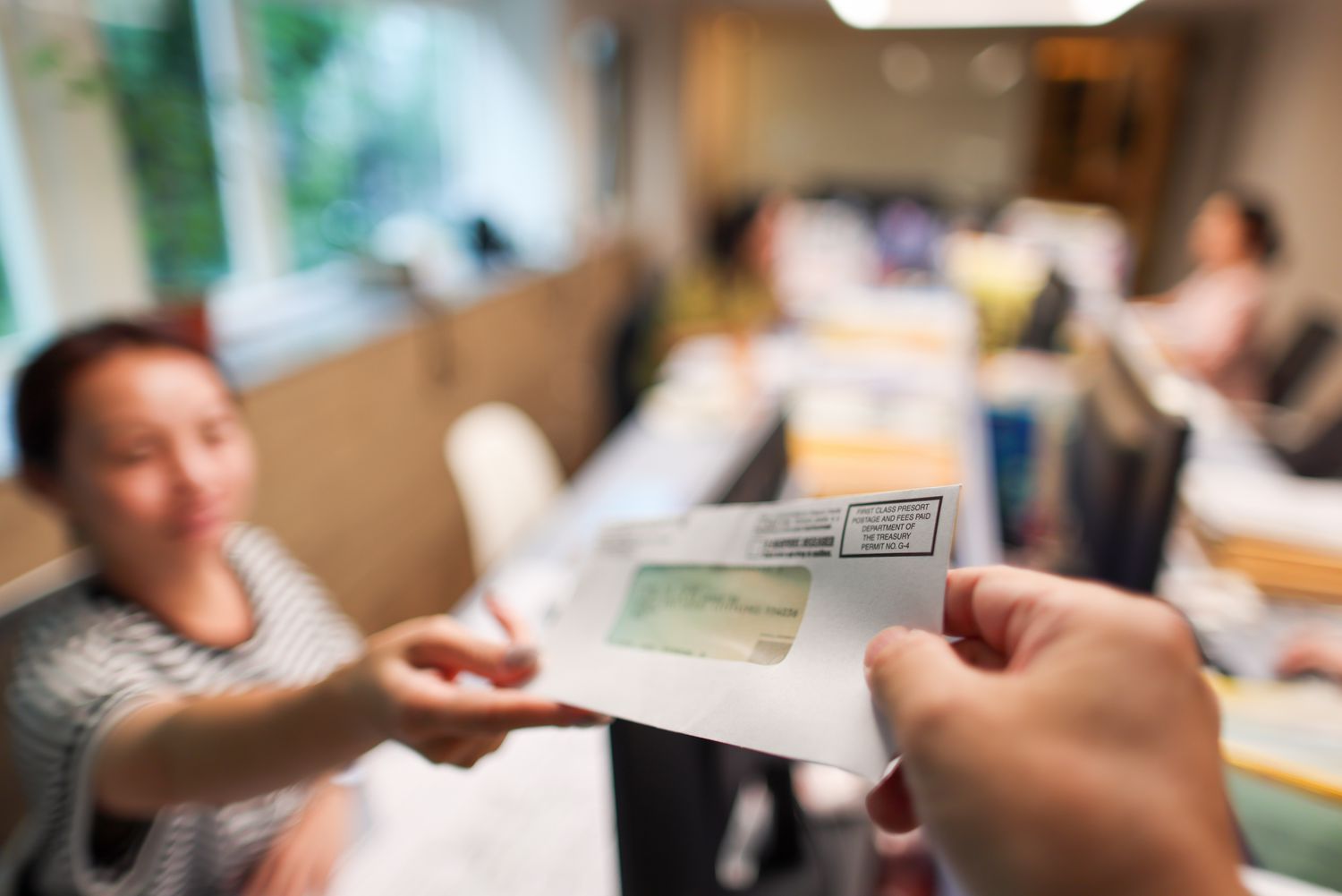 A person receiving a stimulus check in a busy office. Focus is on the check with a blurred background.