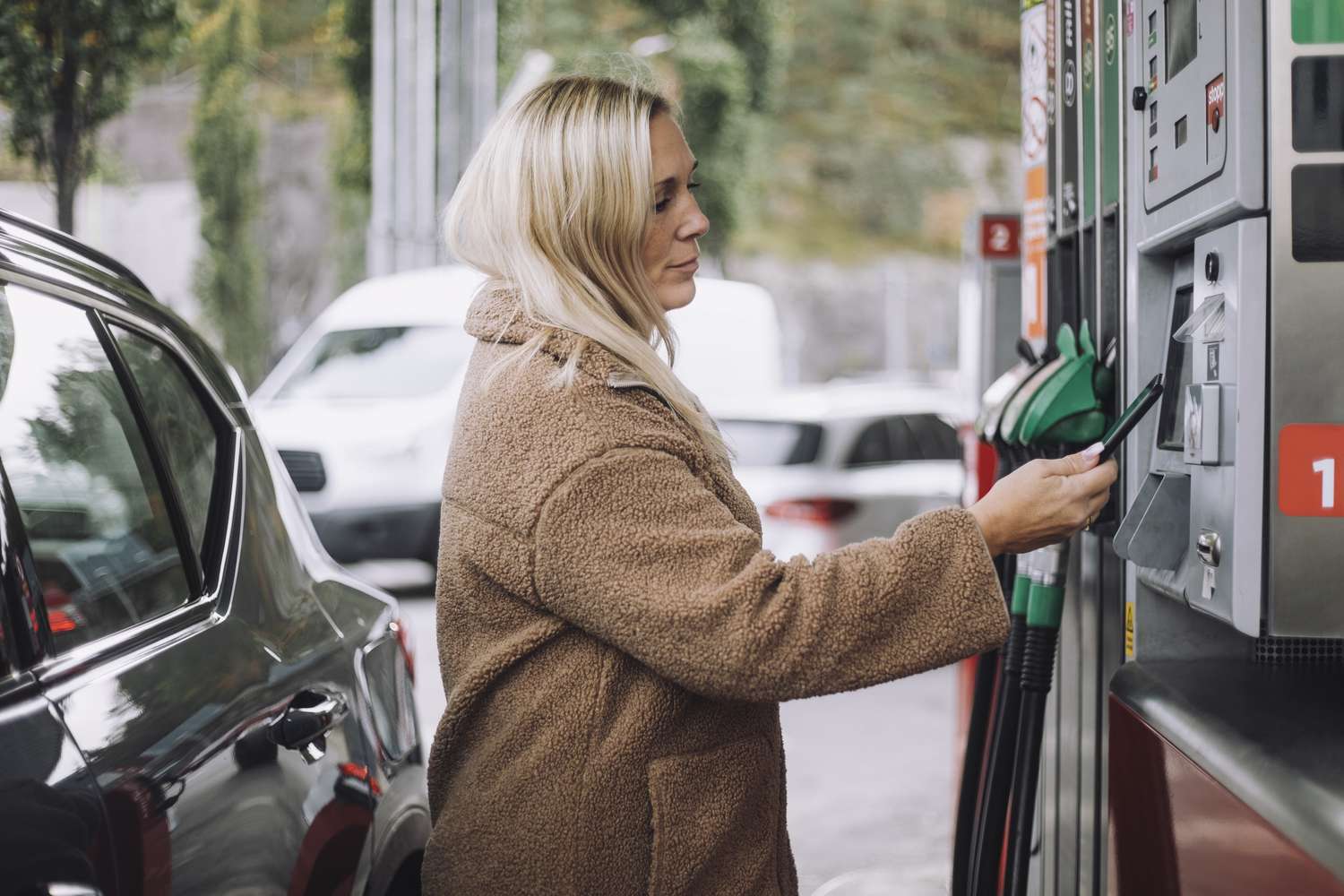 Side view of a woman doing payment via smart phone while standing at fuel station 