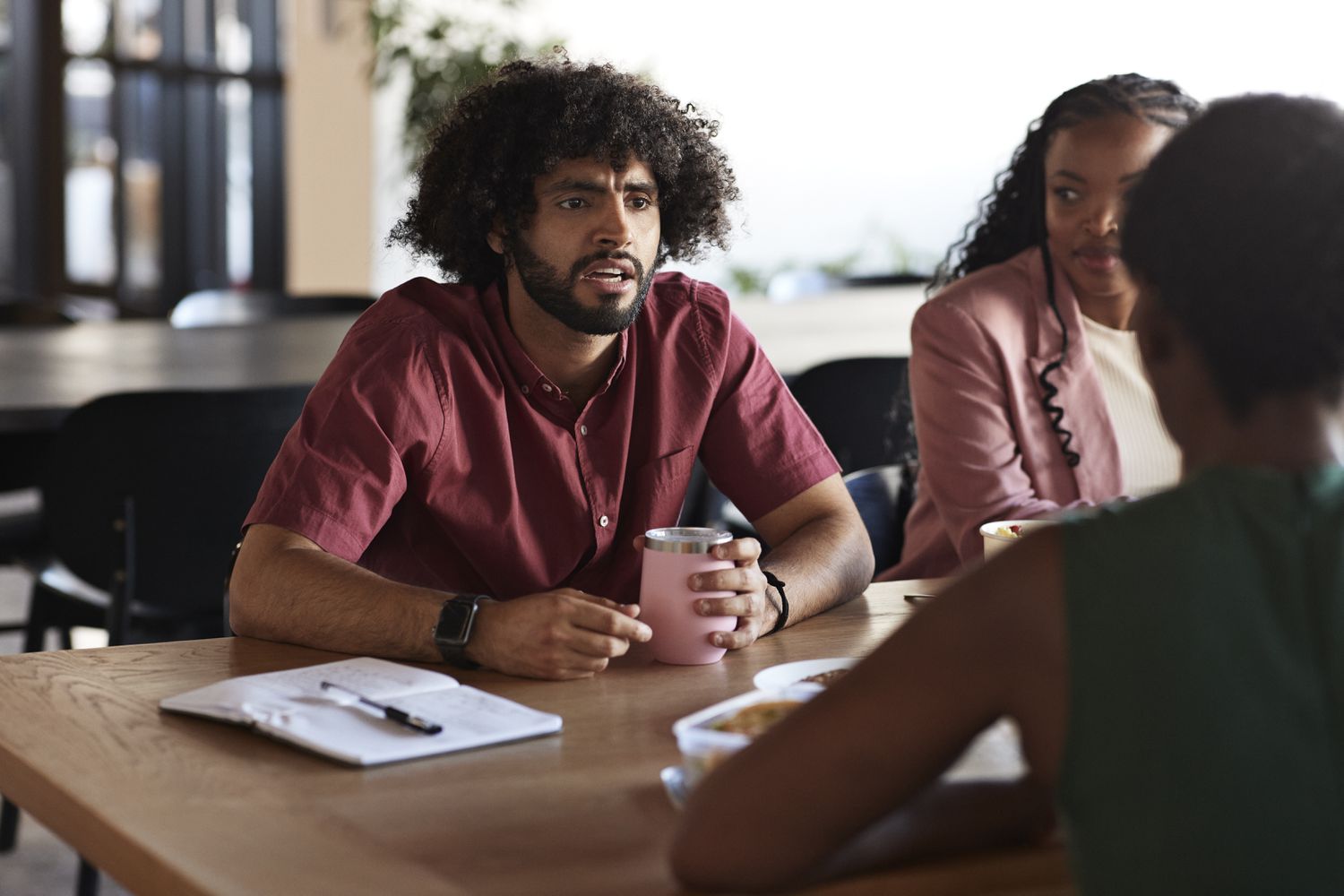 Three people sitting at a table and chatting with food and drinks present