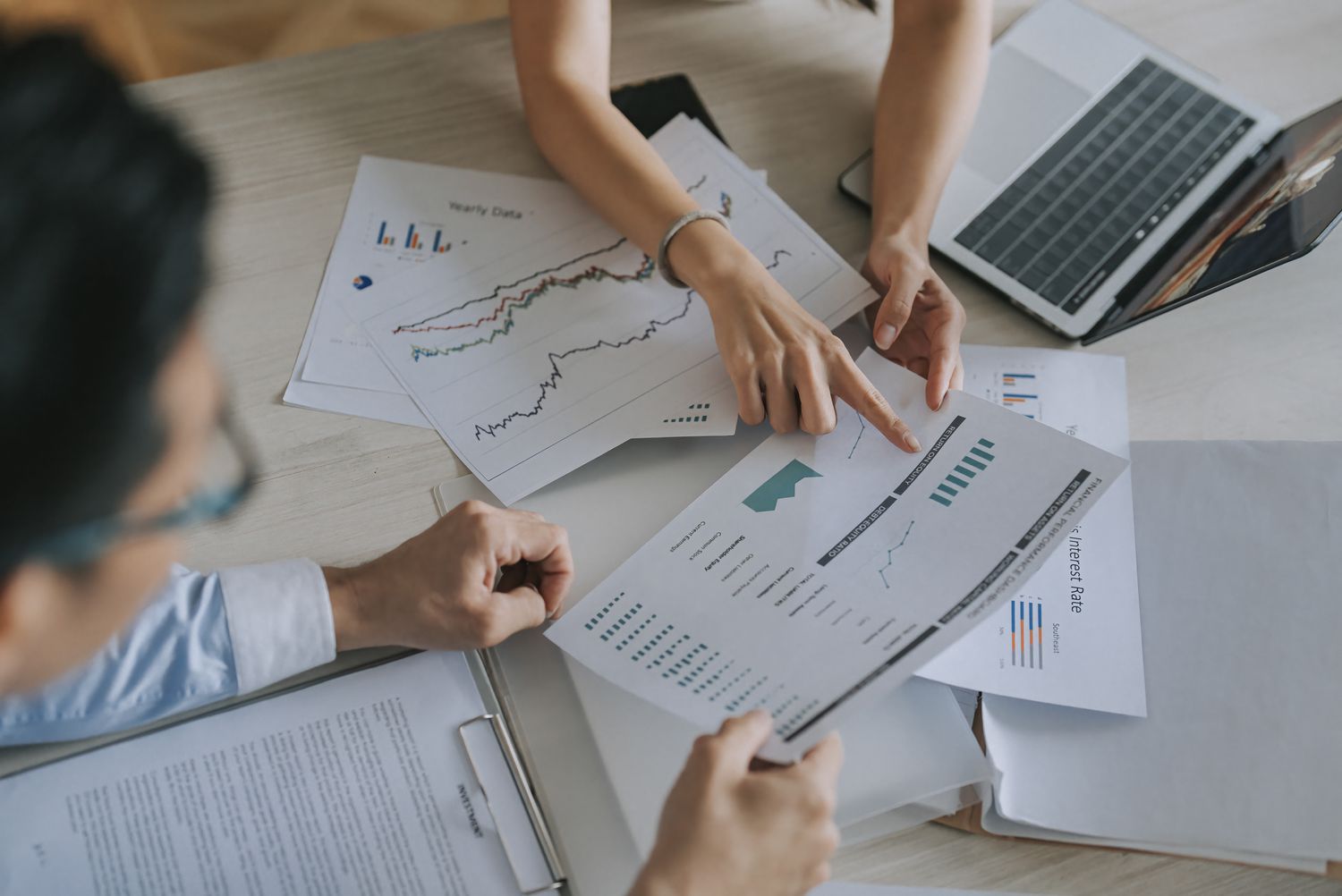 Two coworkers work at a desk discussing business financial reports