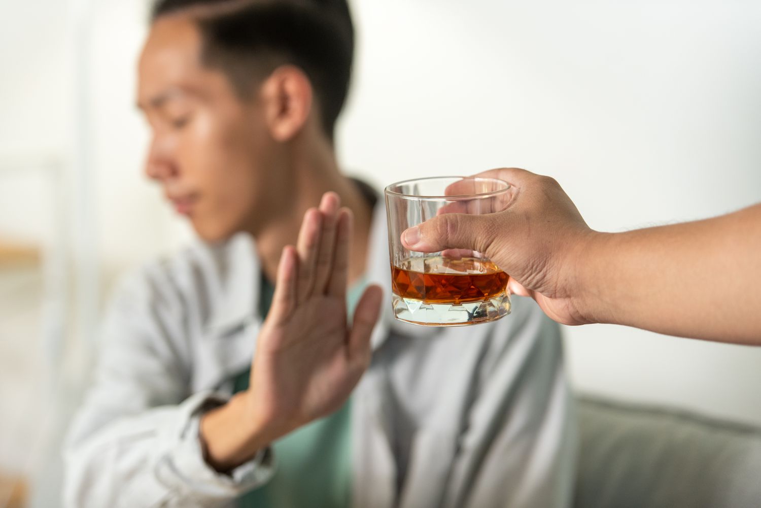 A young man raises his hand to refuse a glass of alcohol offered to him, symbolizing a decision to reject drinking and embrace a healthier lifestyle.
