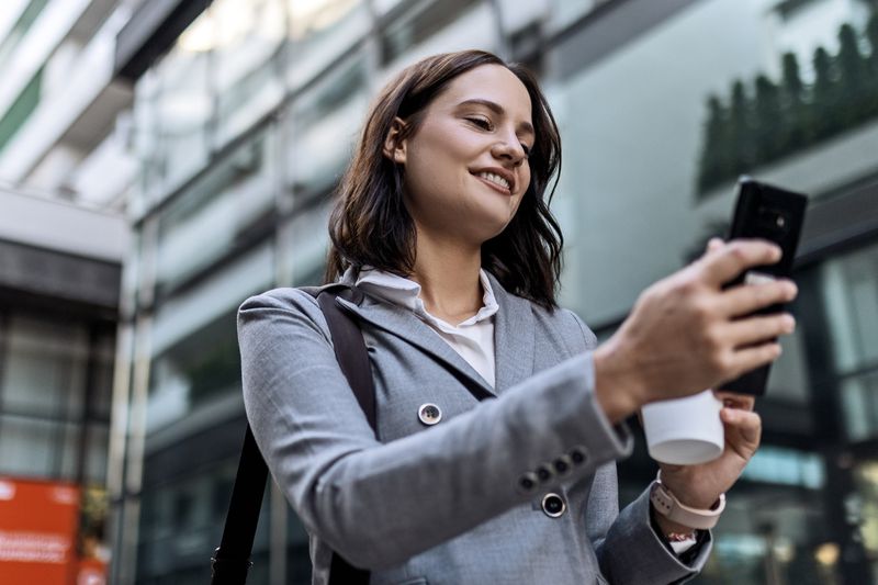 Woman drinking coffee and using mobile phone in front of the office