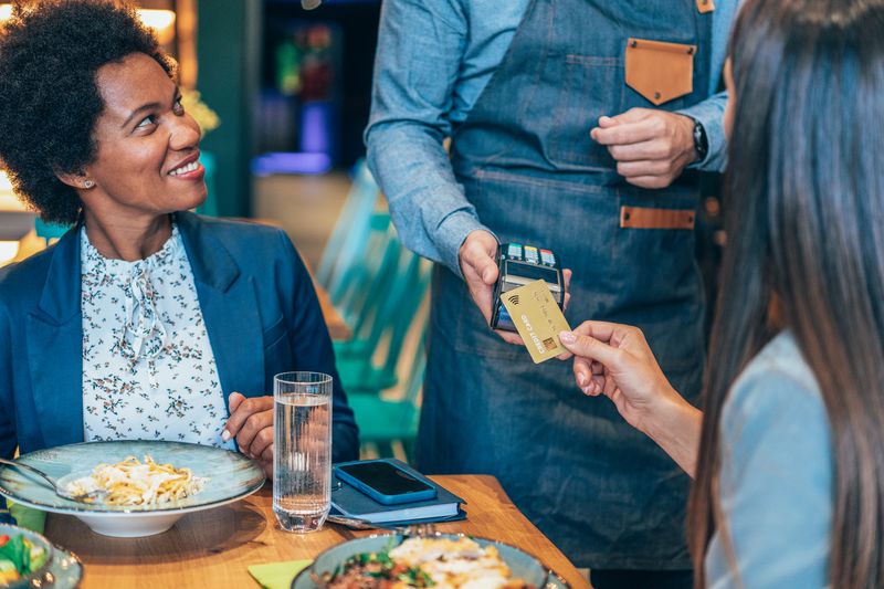 Businesswoman paying for lunch with business colleagues using contactless credit card