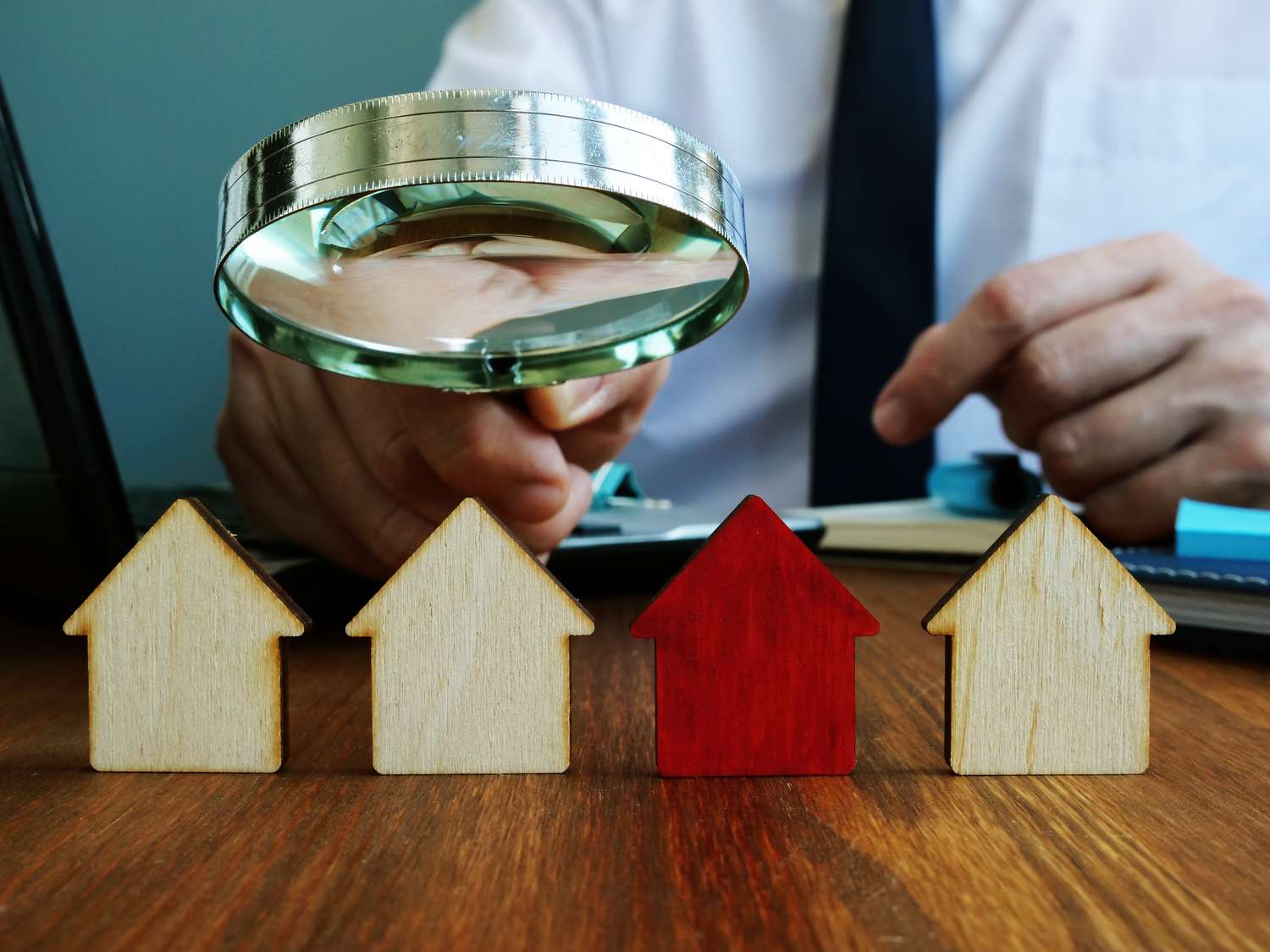 A magnifying glass over small wood depictions of homes.