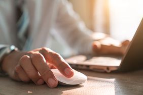 mid-section of a man clicking on a mouse and typing on a laptop