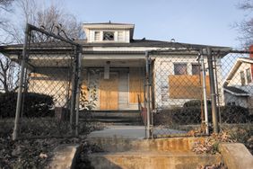 A home with boarded up windows seen through a chain-link fence gate