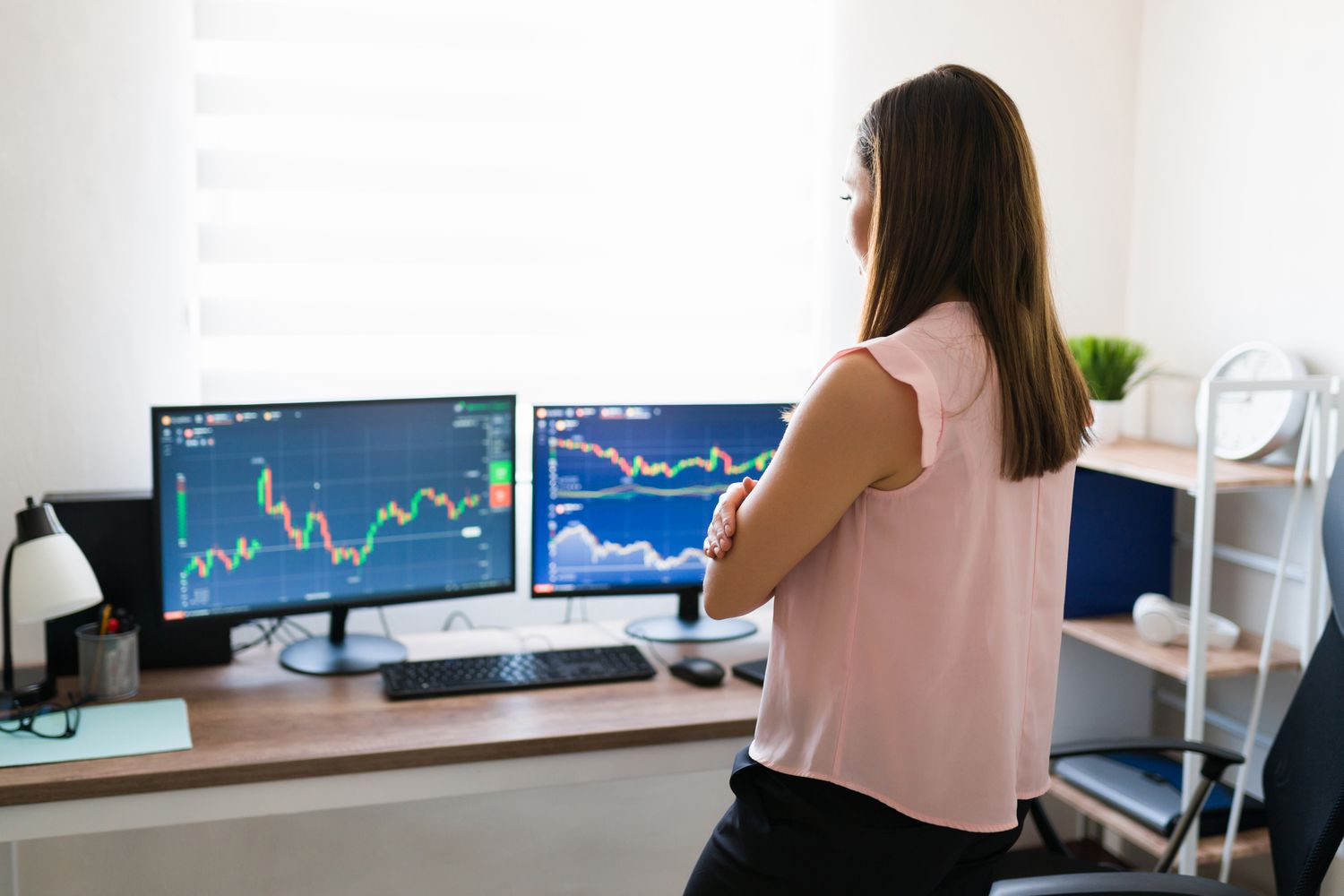 Standing woman looking at charts on two computer monitors