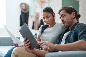 Young couple sitting on their sofa and looking at a mortgage document and a tablet
