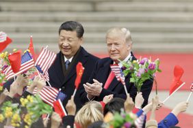 Xi Jinping and Donald Trump among a crowd holding flags and flowers, standing outdoors