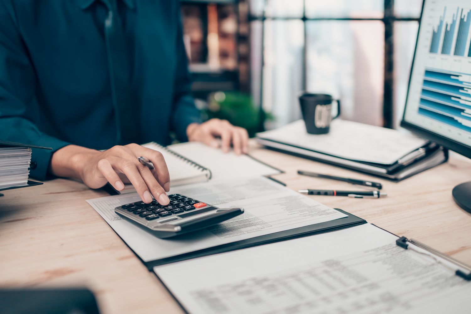 Shot showing hands of a person standing at a desk using a calculator