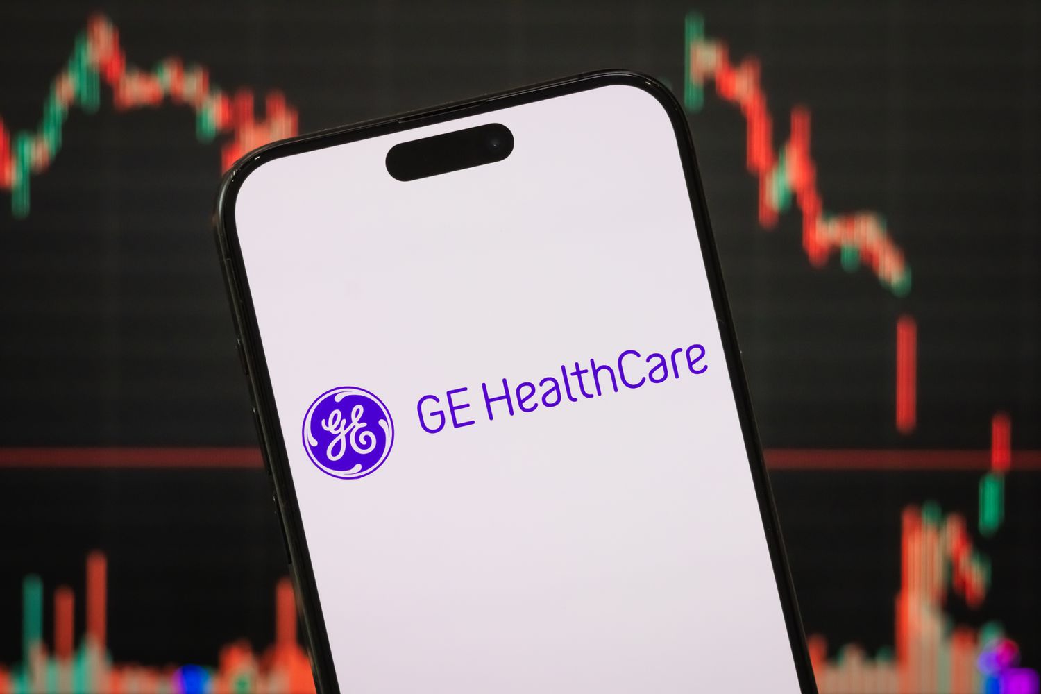 The GE HealthCare logo is seen on a phone screen with a stock chart in the background.