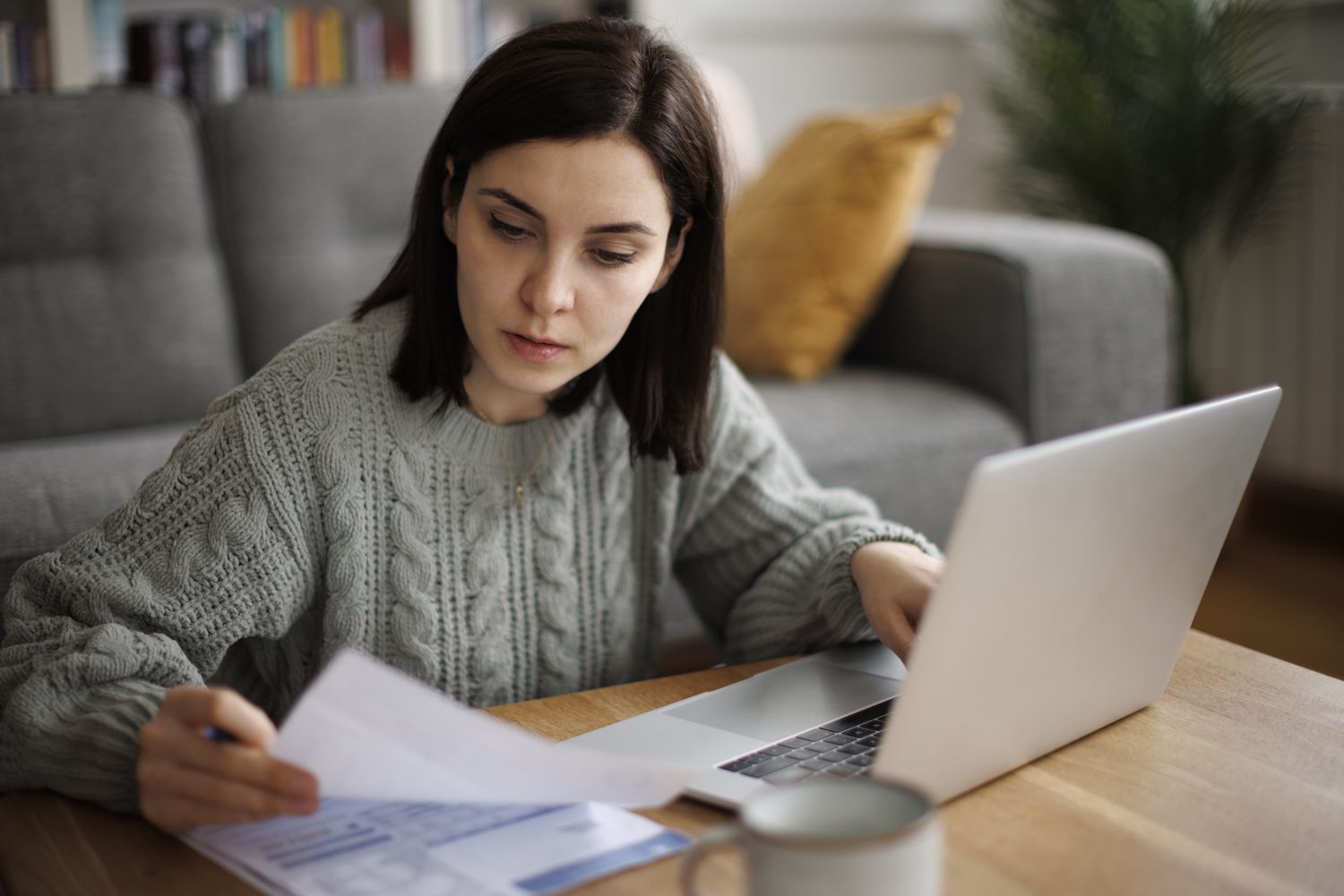 Woman at coffee table looking at papers with an open laptop 