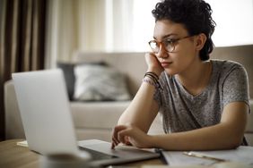 Young woman at home looking seriously at bank rates on her laptop
