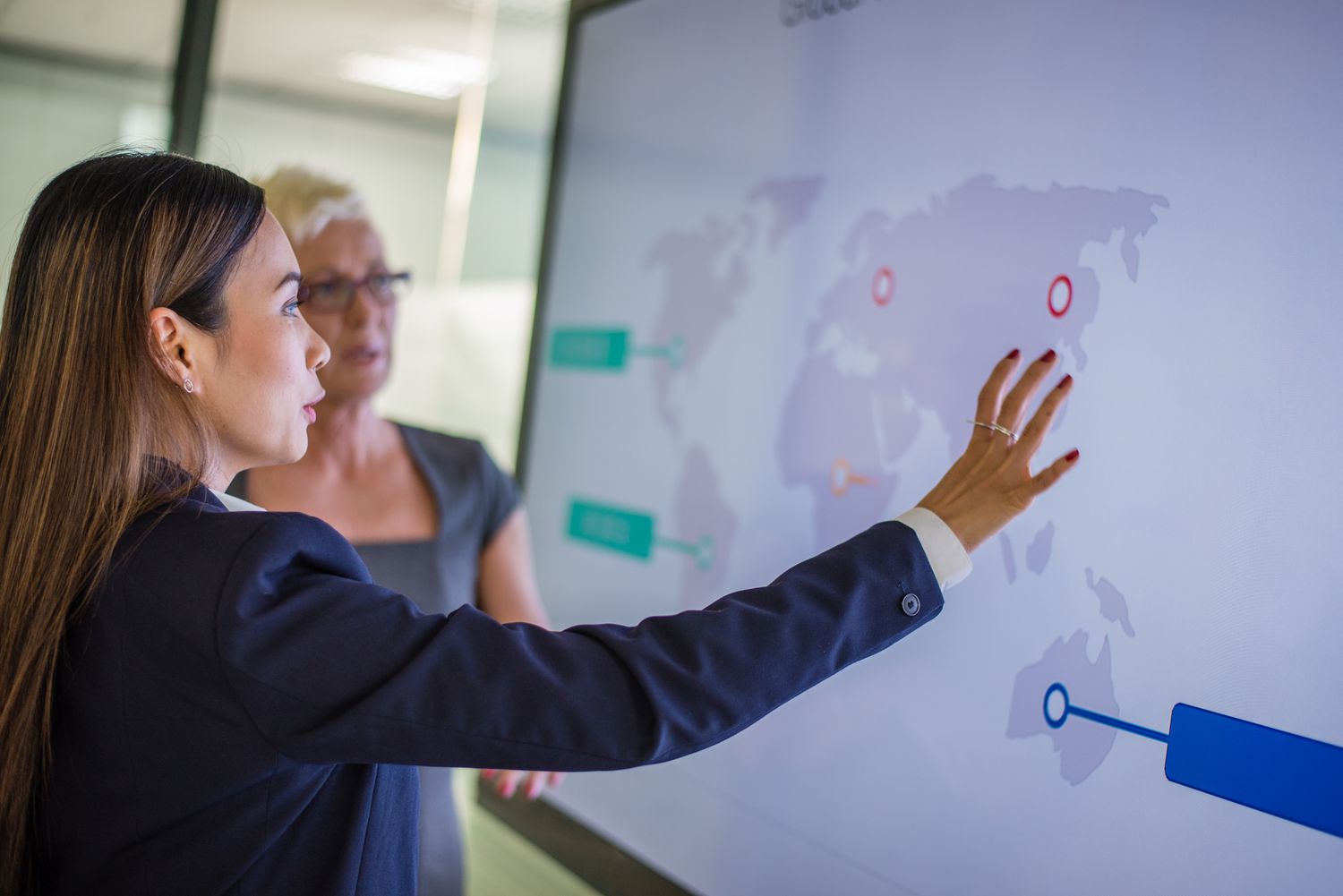 Two foreign business executives look at a large map of the world showing stock markets where their company shares are listed.