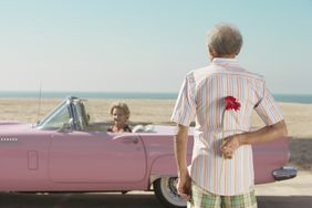 An older person, flower behind their back, looking at a date seated in a pink cadillac.