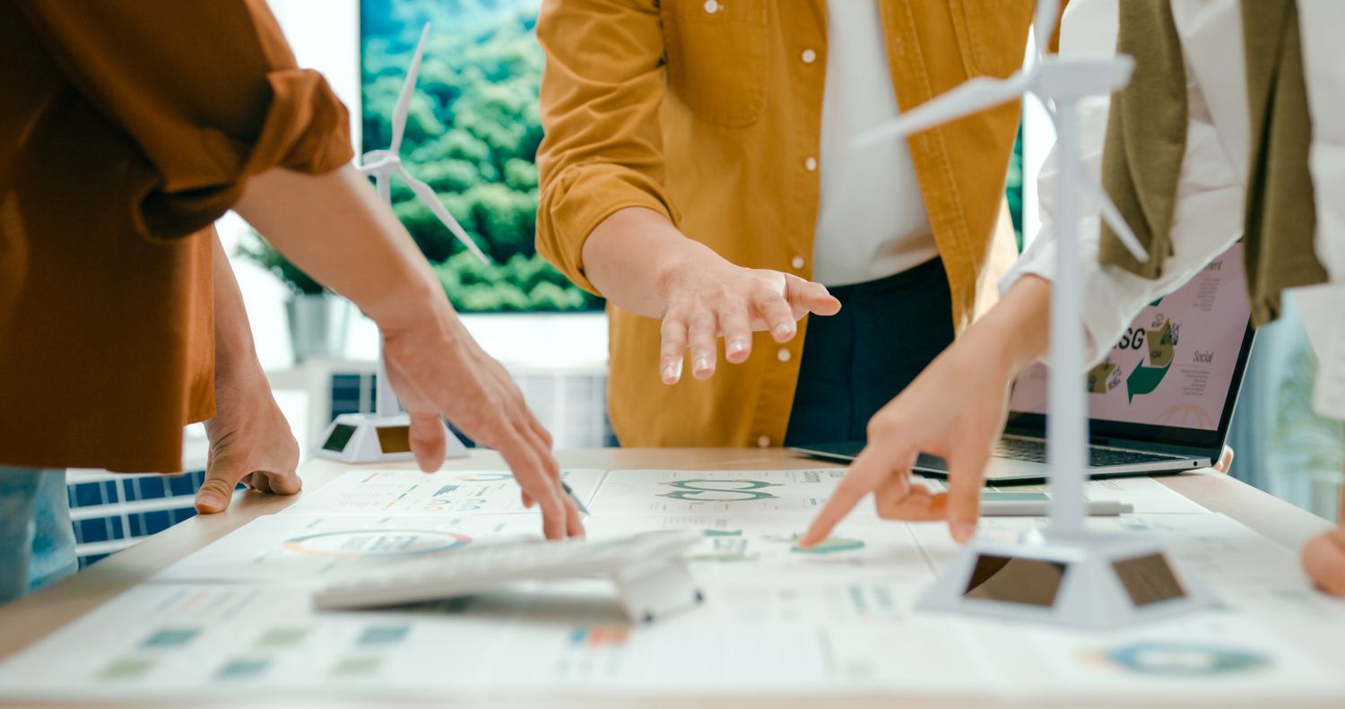Close up of the hands of co-workers pointing to a large document lying on a table.