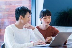 Young couple sitting at home and looking together at mortgage refinance rates on a laptop