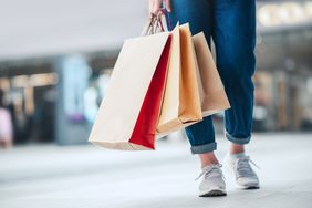 Bottom cropped legs of a person wearing jeans and sneakers and holding three paper shopping bags