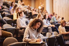 A stock image of a female student in a lecture hall, with other students in the background. 