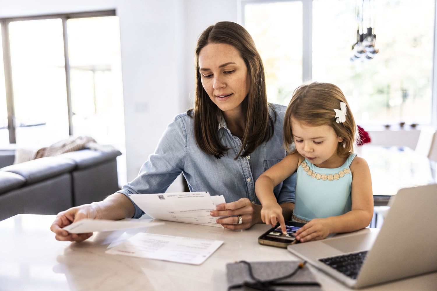 Mother looking through paperwork while young child is sitting on her lap.