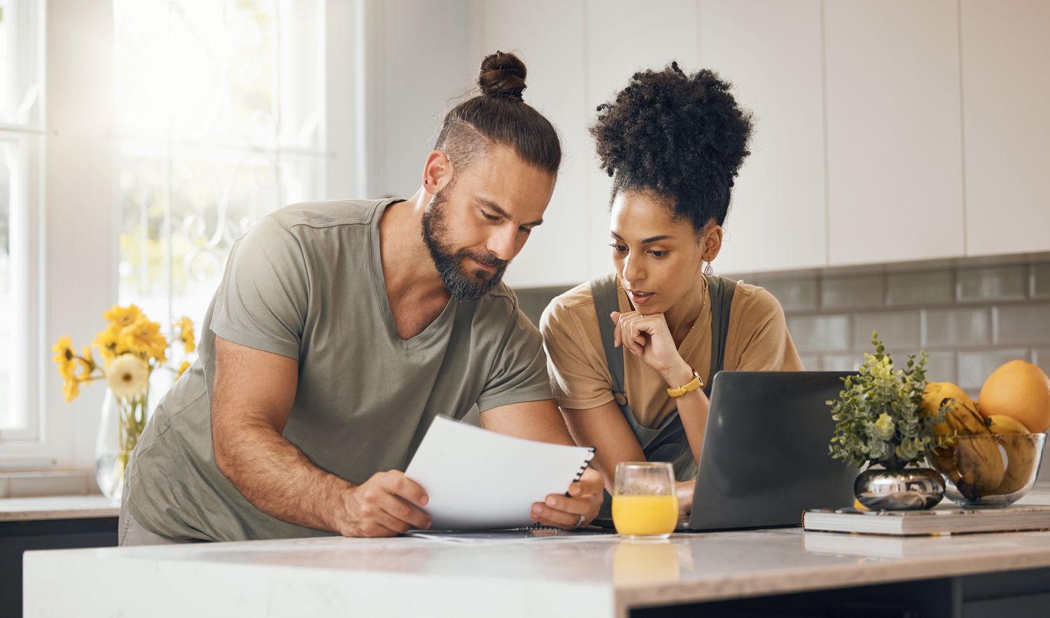A young couple reviews documents and comparing mortgage rates in a kitchen.