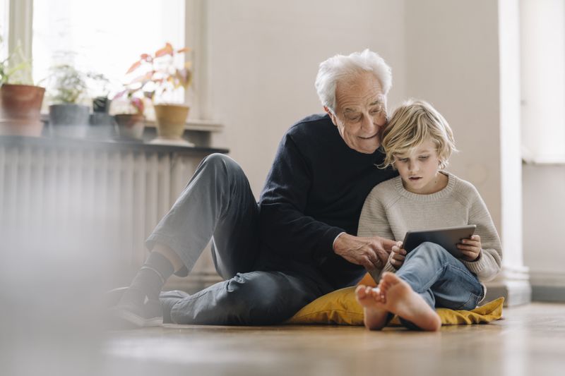 An older man sits on the floor with a young boy.