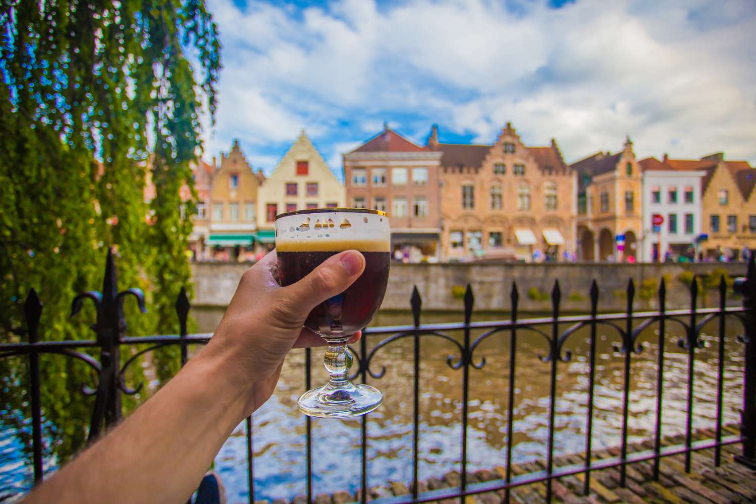 Full glass of beer on Brugge cityscape background. Hand with beer glass in Bruges, Belgium.