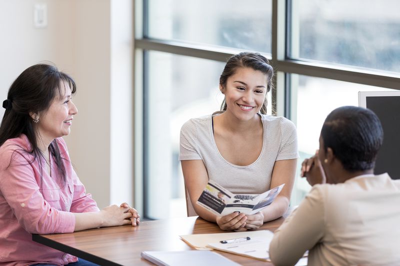 Young woman and her mother talk with a female bank employee about a student loan