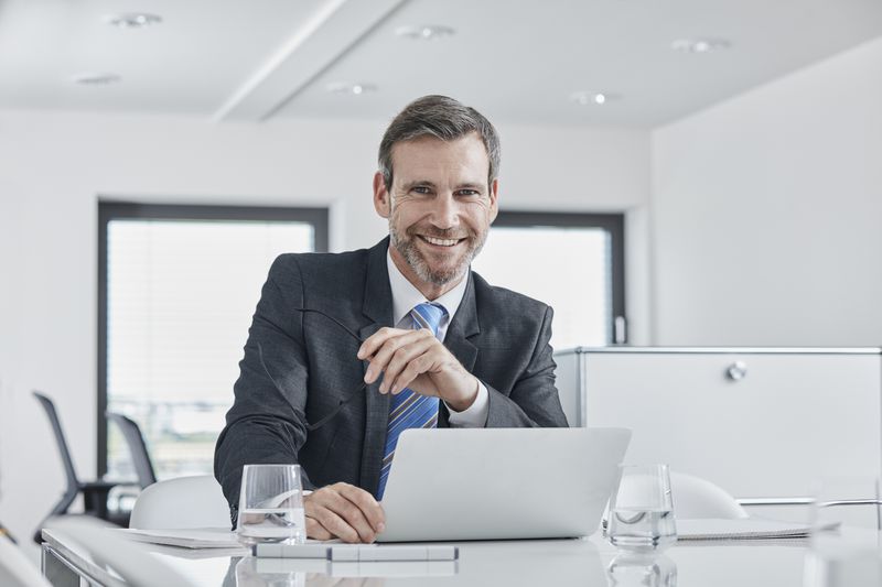 A smiling businessman with laptop at desk in office.