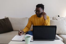 A person sitting at home and noting down ways to improve the current fair credit score to a good credit score.