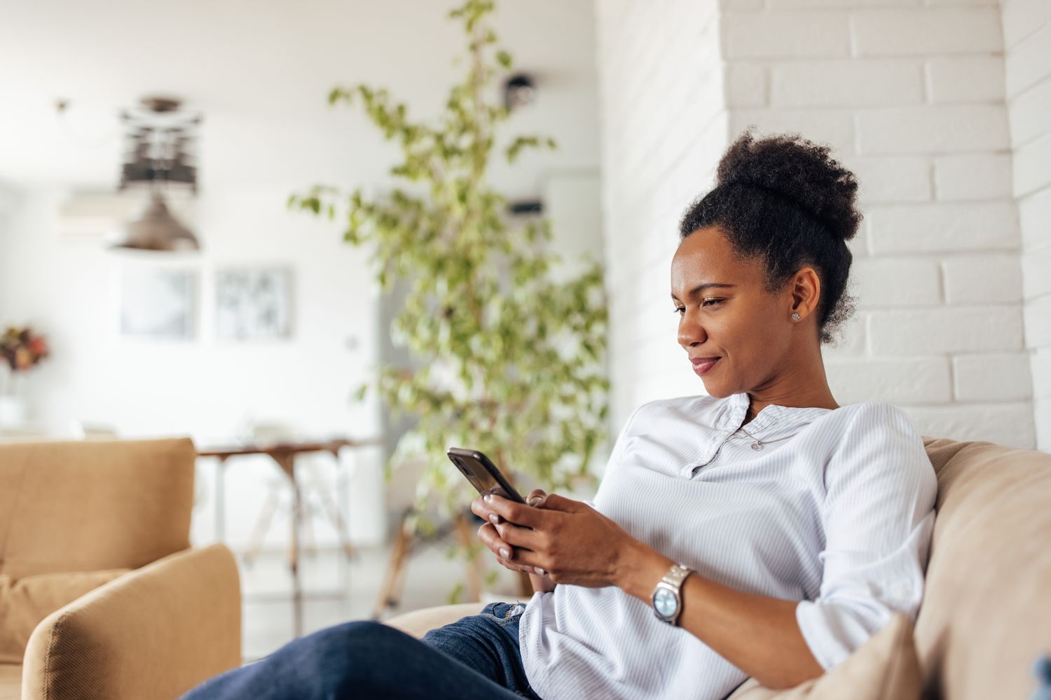 Young woman sitting in her living room and pondering something on her smartphone