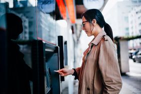 A young woman inserts her card into an ATM on a city street.