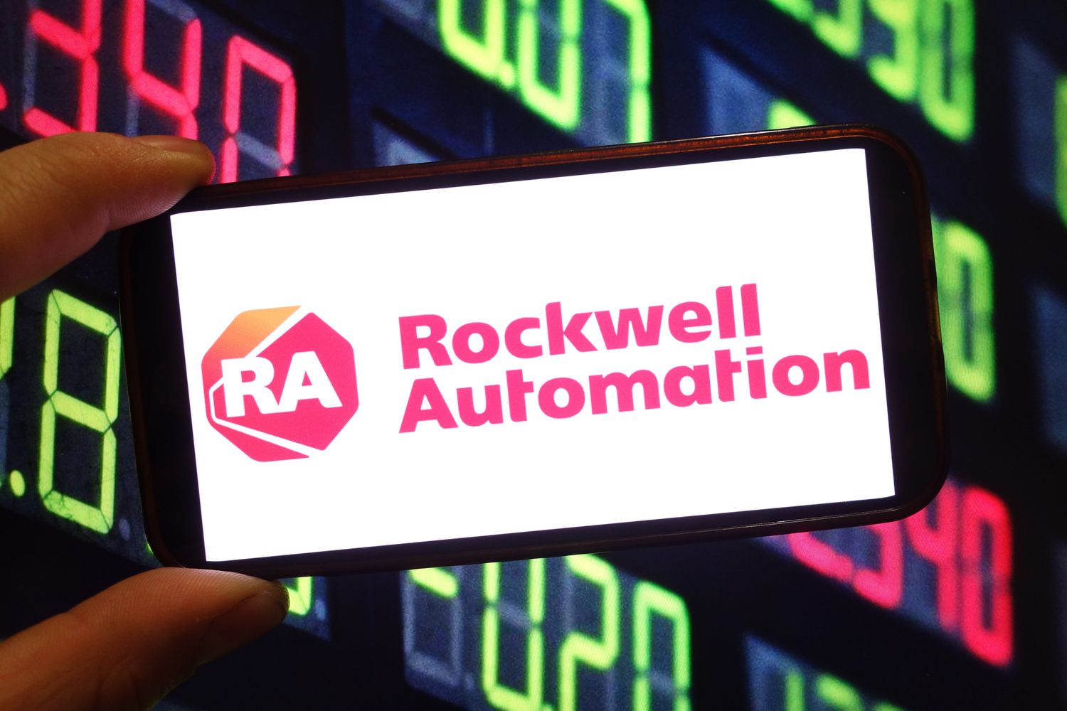 The red Rockwell Automation logo is seen on a phone screen, with green and red numbers in the background.