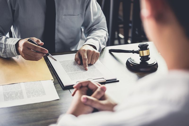 The Midsection of Judge Pointing at Document While Worried Client Sitting on Table