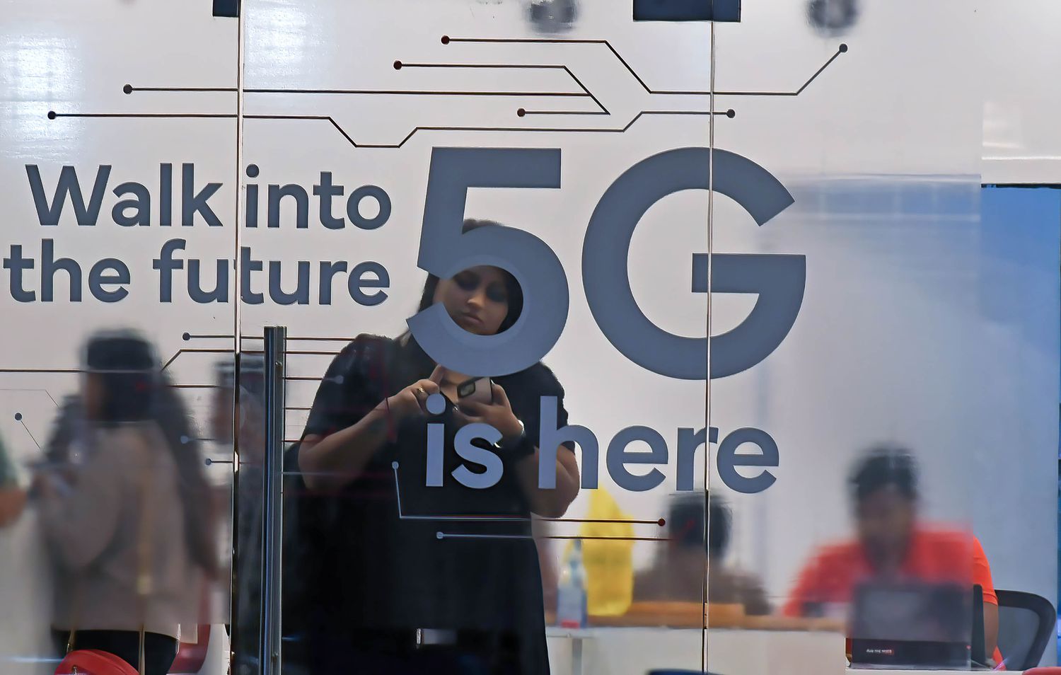 A person checks their mobile phone inside a mobile service provider store advertising 5G service.