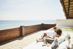 Wide shot of couple relaxing on deck of luxury tropical villa overlooking ocean
