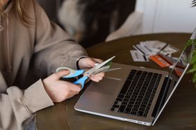 A person cutting credit card with scissors to avoid spending instead of closing the credit card.