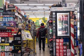 Person walking down an aisle in a store, surrounded by shelves of products and a Coca-Cola display in the foreground