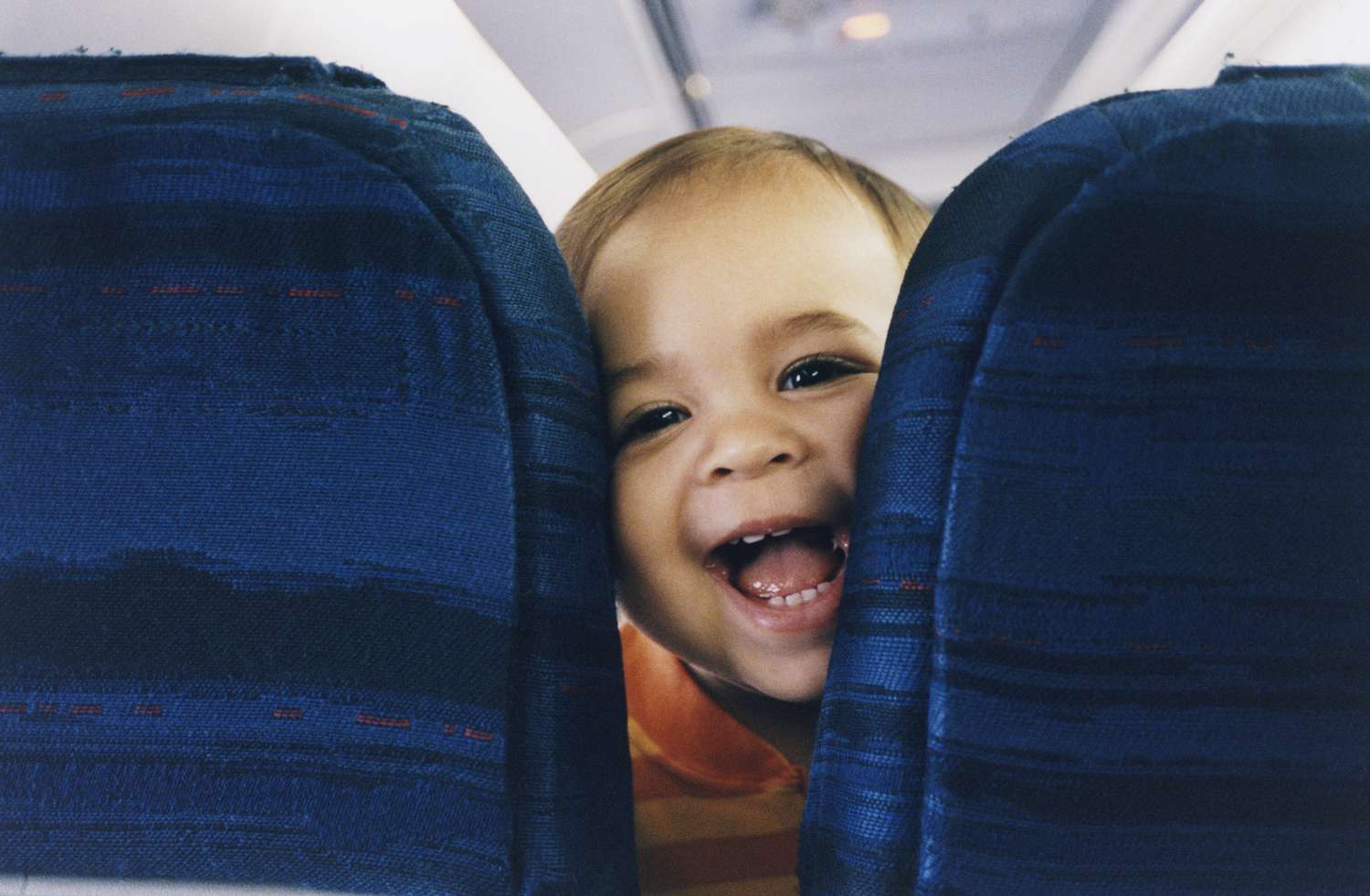 Baby's face squished between two airplane seats looking straight at the camera