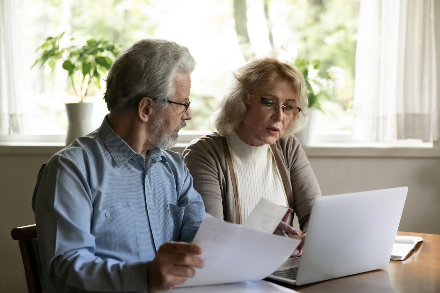 Older couple sitting in their kitchen and looking together at mortgage documents and a laptop