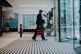 A smartly dressed man walks towards revolving doors in a modern office building.