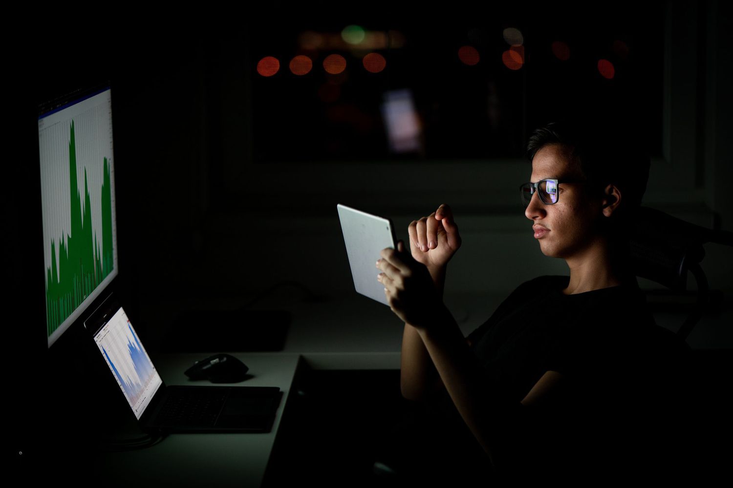 Young man looking at a tablet in front of a computer showing financial information